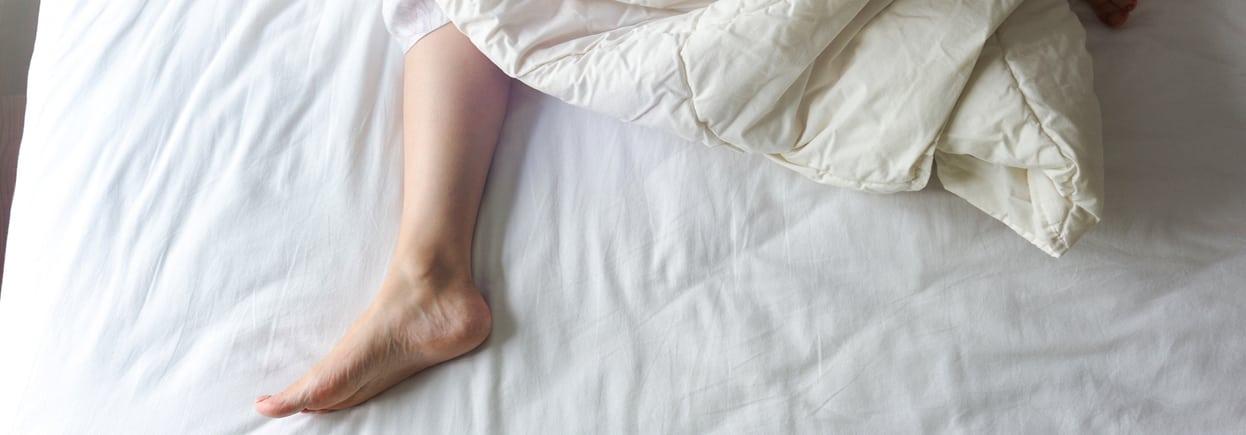 Bare Feet of a Young Woman on White Bed