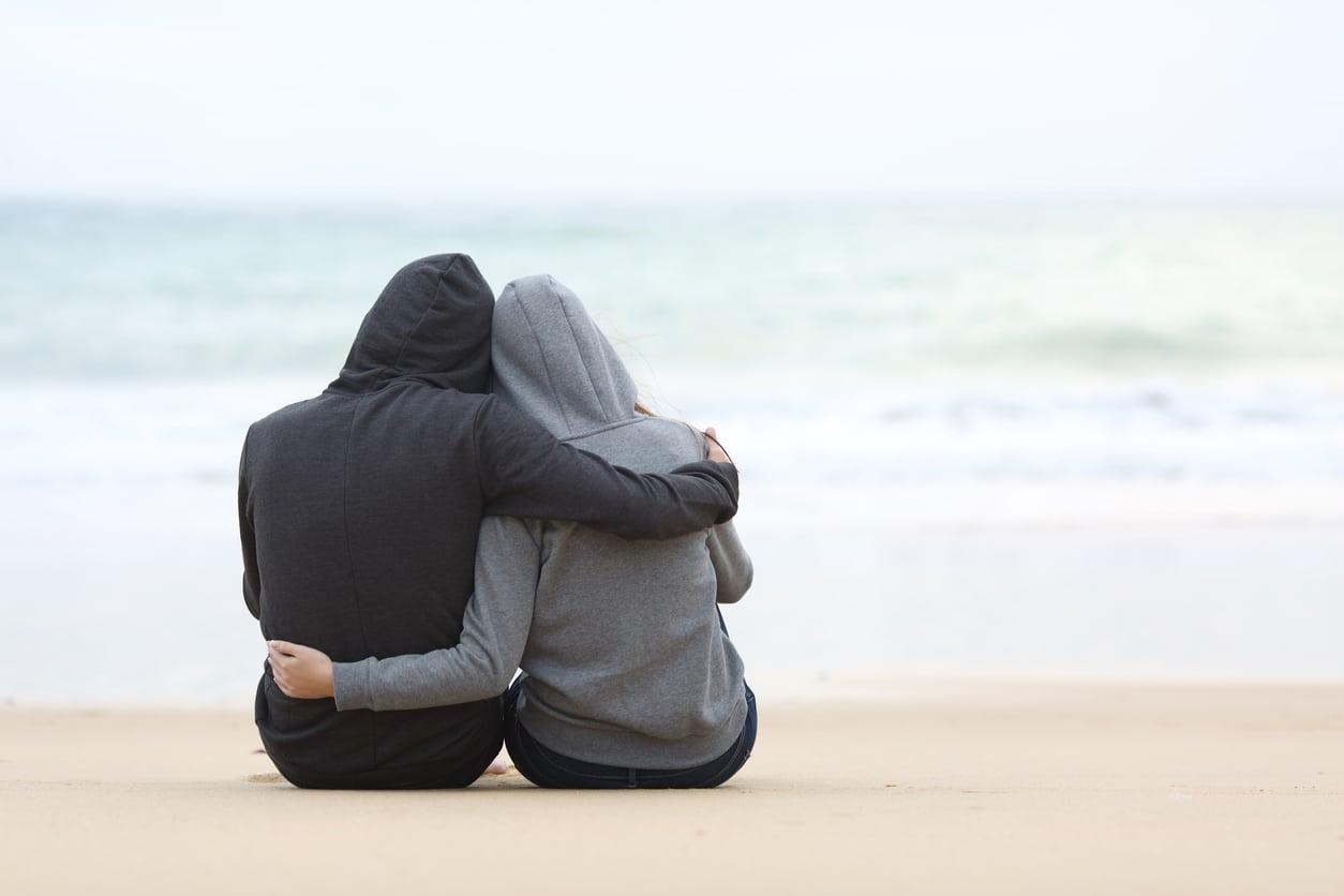 Couple of teenagers hugging watching sea