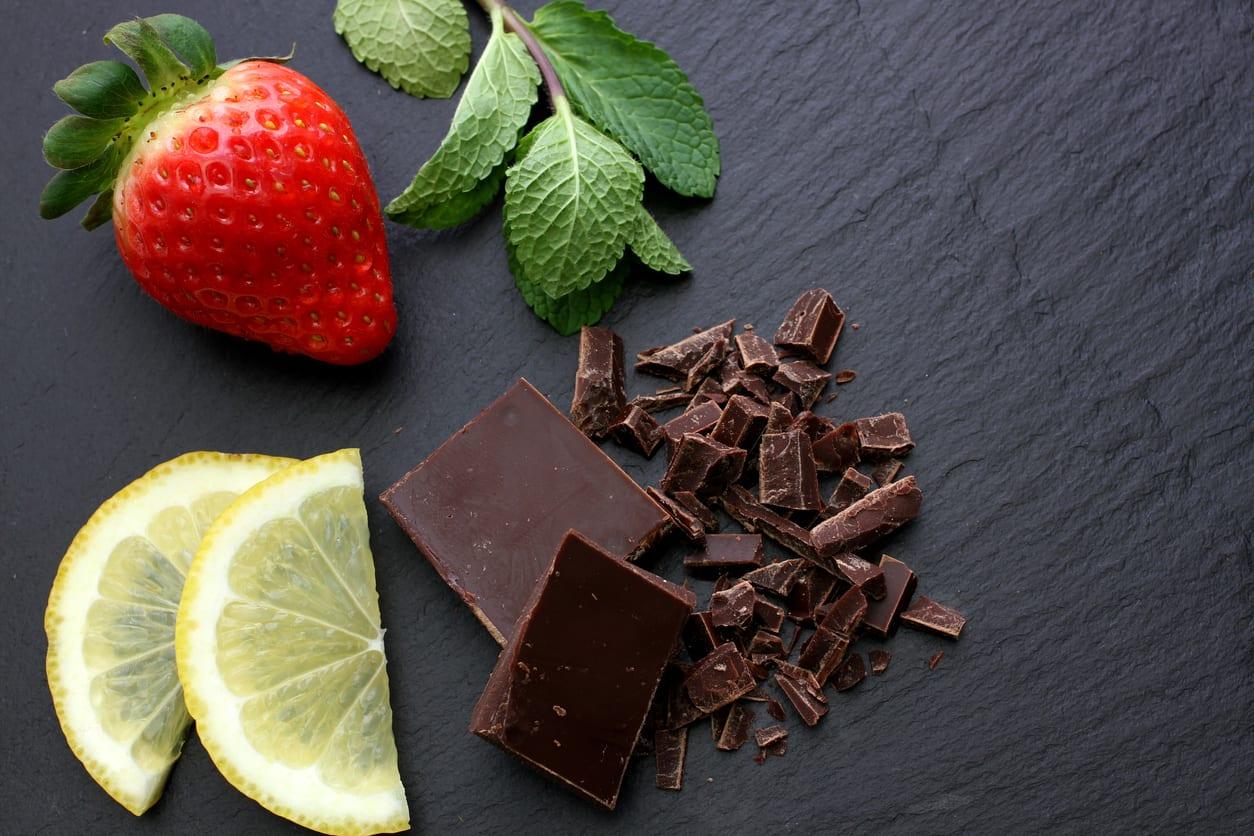 Strawberry, lemon slices, mint leaves and black chocolate on black slate background