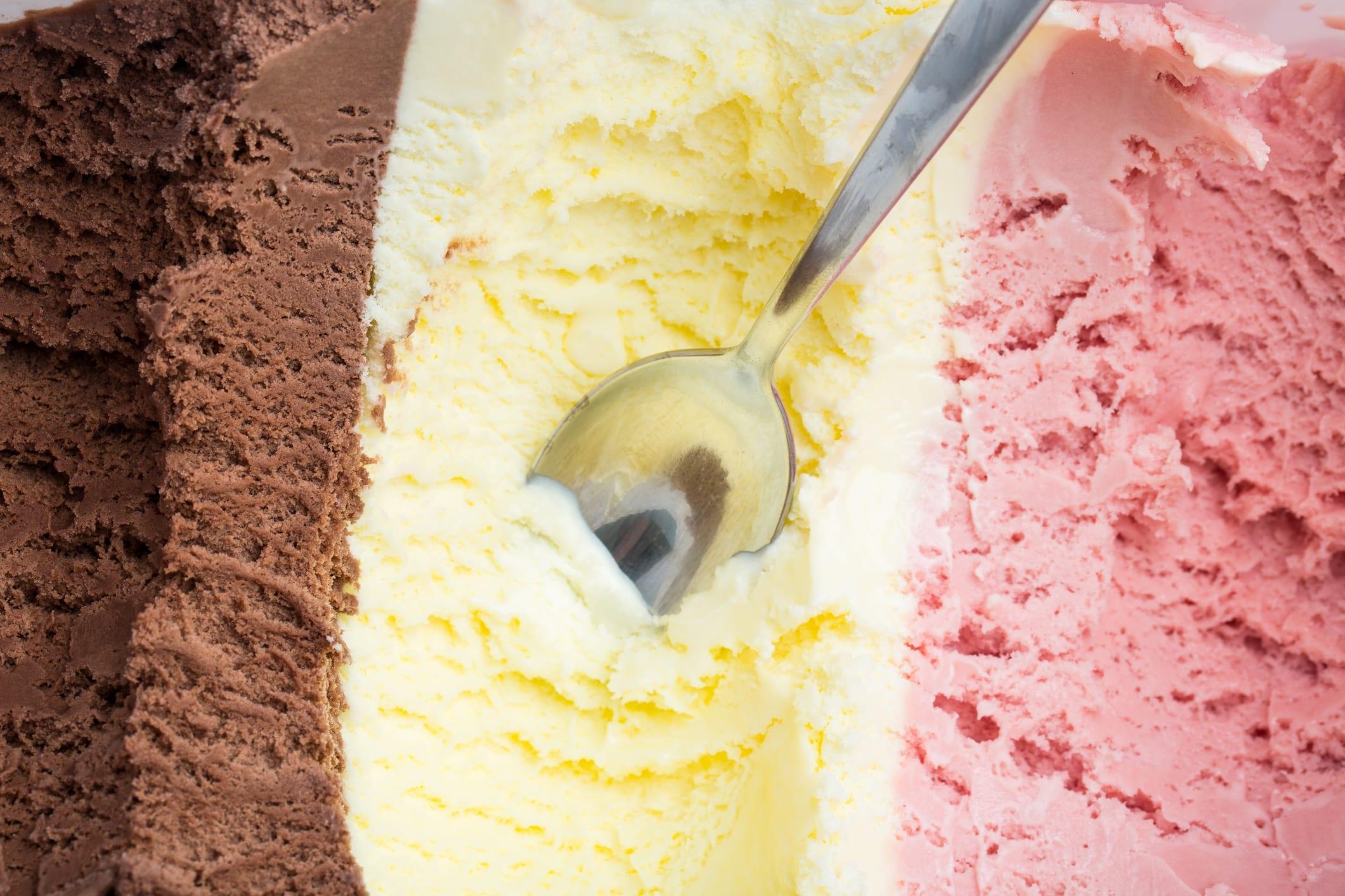 ice cream: A spoon in a large ice box with chocolate, vanilla and strawberry ice cream